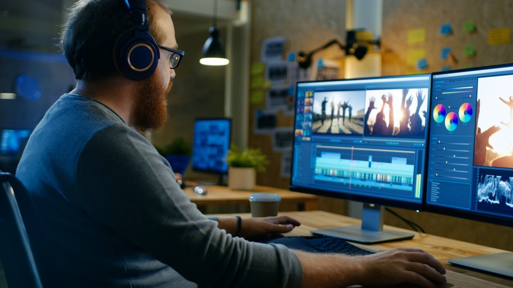 Male Videographer Edits and Cuts Footage and Sound on His Personal Computer, Puts on His Monitors/ Headphones. His Office is Modern and Creative Loft Studio.